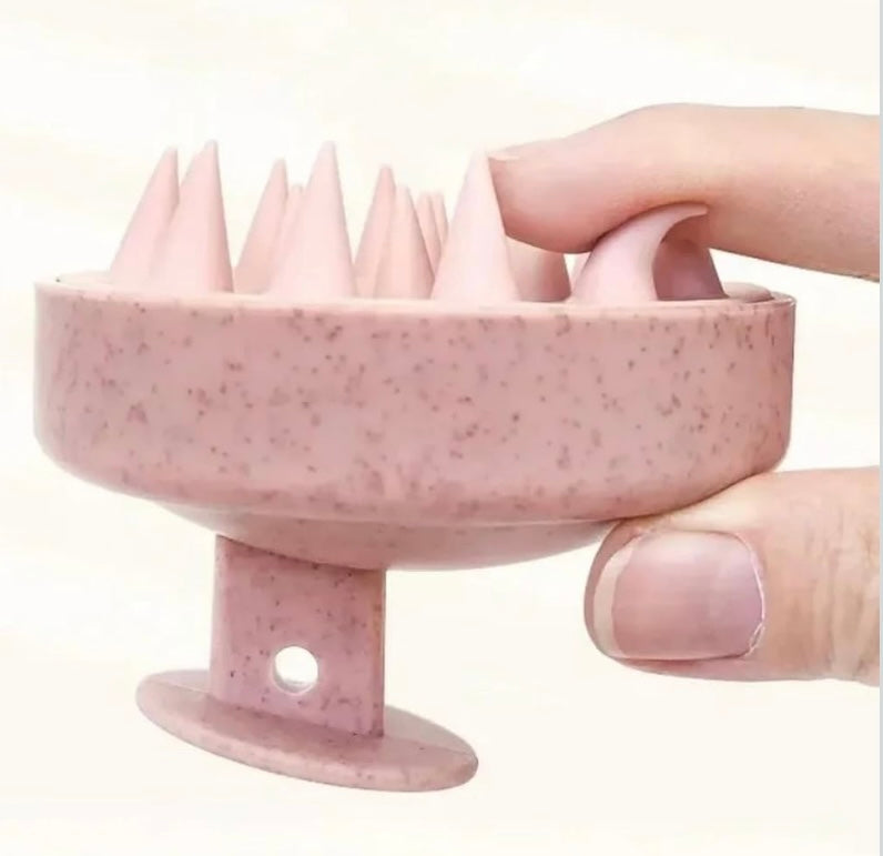 Pink textured scalp massager with a hand holding it against a white background