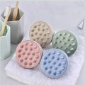 Four round, textured silicone scalp scrubs in pastel colors on a towel.