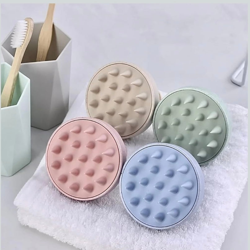 Four round, textured silicone scalp scrubs in pastel colors on a towel.